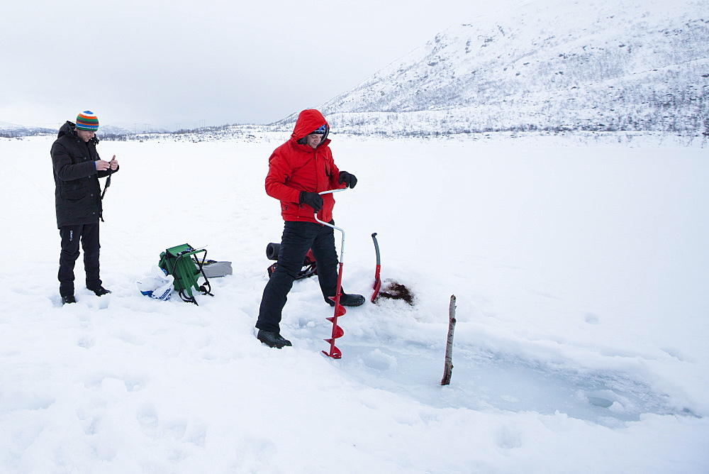 Drilling a hole in the ice while fishing on frozen lake in the Arctic Circle on Ringvassoya Island in the region of Tromso, Northern Norway