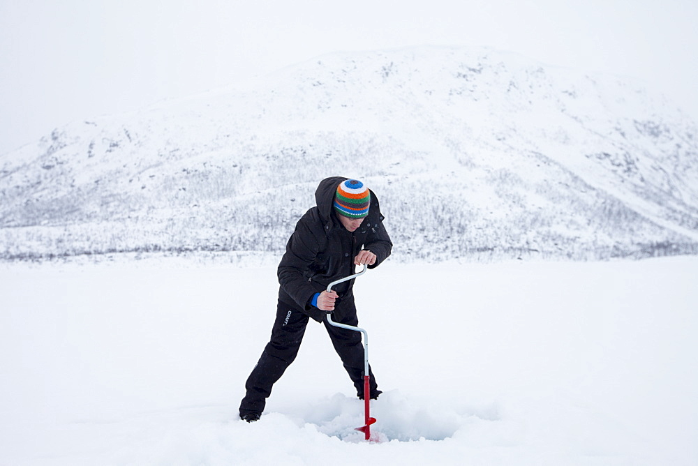 Drilling a hole in the ice while fishing on frozen lake in the Arctic Circle on Ringvassoya Island in the region of Tromso, Northern Norway