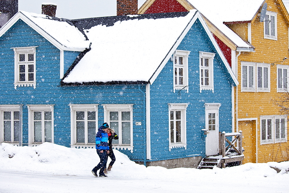 Couple walk past traditional wooden buildings along Storgata in the quaint area of Tromso, in the Arctic Circle in Northern Norway