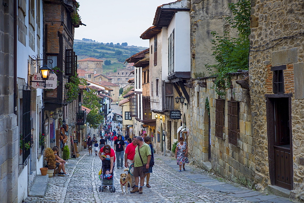 Tourists and residents pass medieval houses in cobbled street of Calle Del Canton in Santillana del Mar, Northern Spain