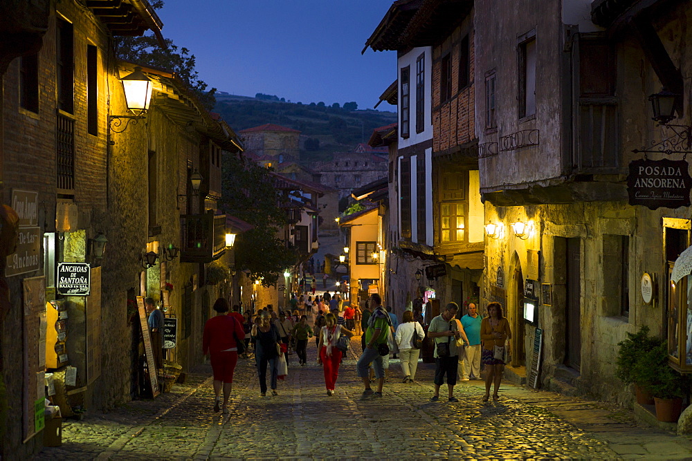 Tourists stroll at night past medieval buildings on cobbled street of Calle Del Canton in Santillana del Mar, Cantabria, Spain