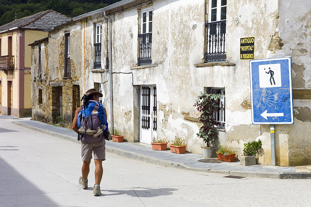 Walker checks sign on Camino de Santiago Pilgrim's Walk, to Santiago de Compostela at Triacastela in Galicia, Spain