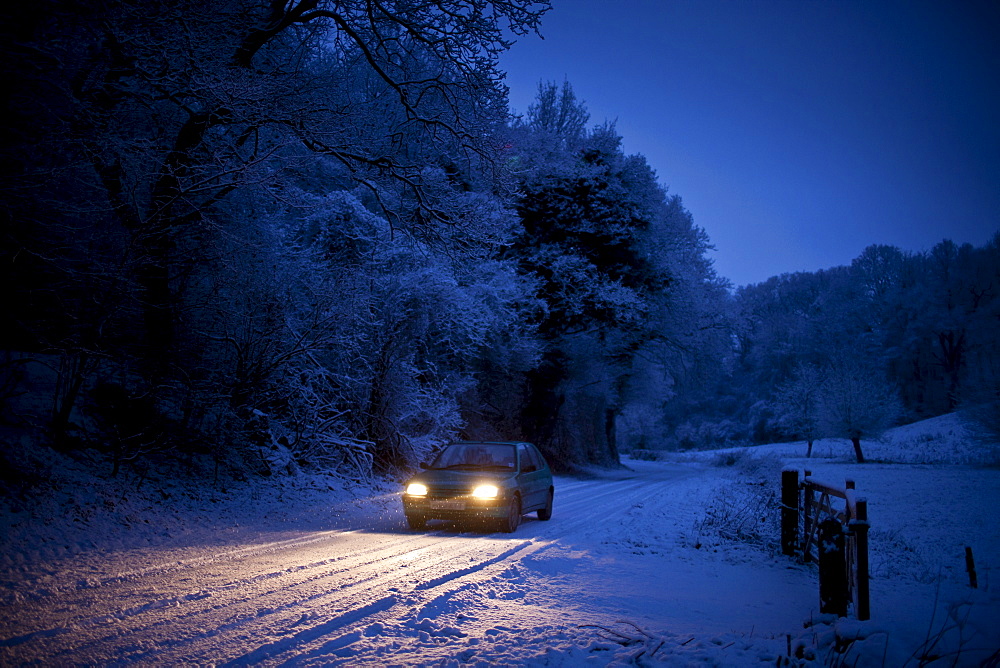 Small car drives slowly on icy road in The Cotswolds, Swinbrook, Oxfordshire, United Kingdom