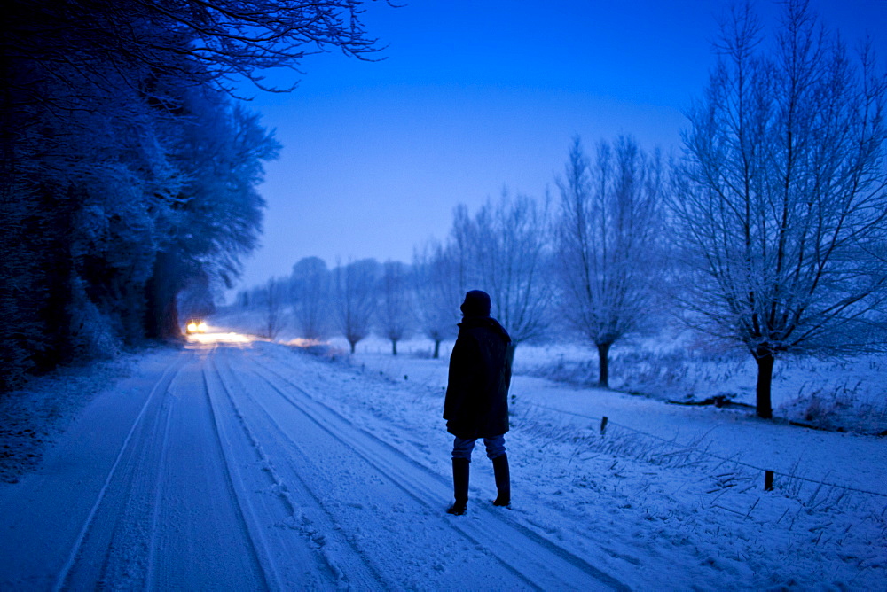 Lone walker in traditional snow scene in The Cotswolds, Swinbrook, Oxfordshire, United Kingdom