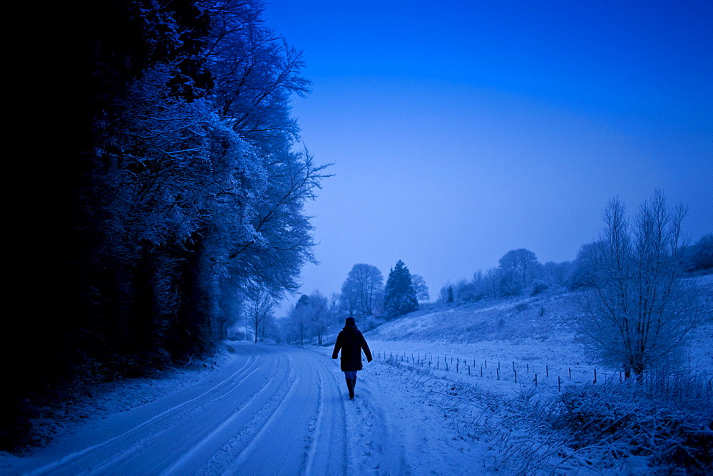 Lone walker in traditional snow scene in The Cotswolds, Swinbrook, Oxfordshire, United Kingdom