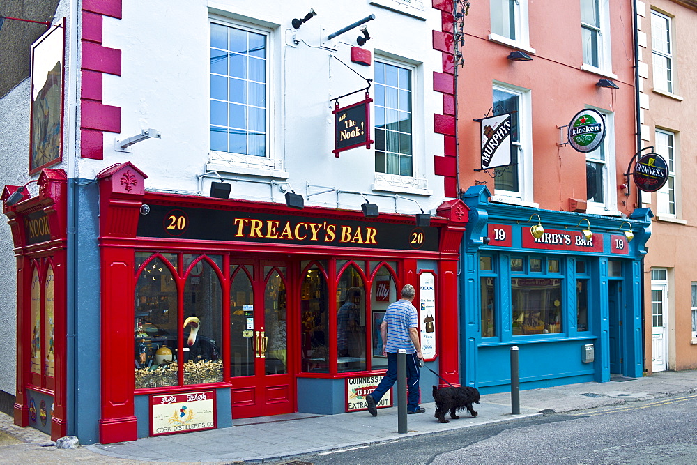 Man walking dog past Treacy's Bar and Kirby's Bar in Youghal, popular tourist town in County Cork, Ireland