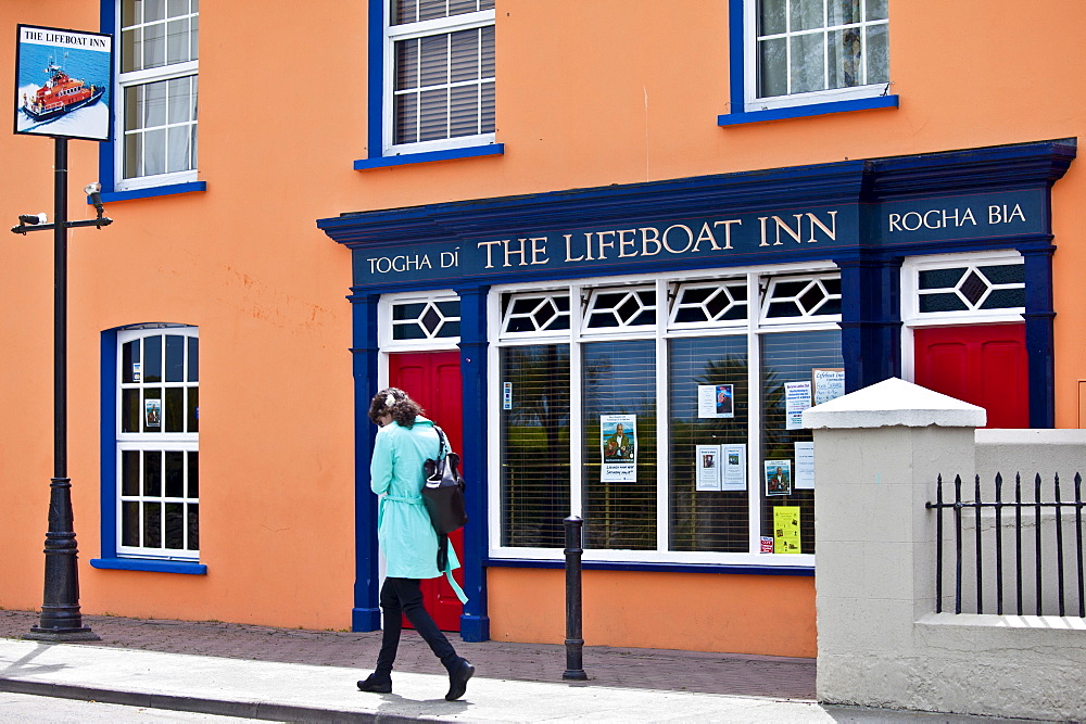 Young woman strolls past The Lifeboat Inn traditional bar in Courtmacsherry, West Cork, Ireland