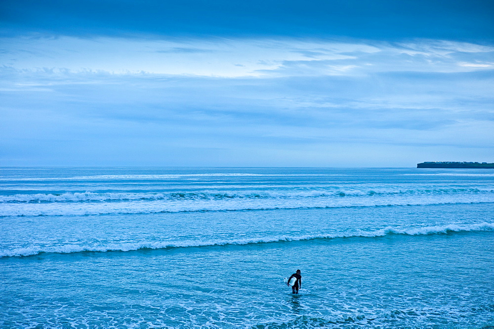 Lone surfer leaving the surf at high tide at beach resort of Lahinch (Lehinch) at twilight, County Clare, West Coast of Ireland