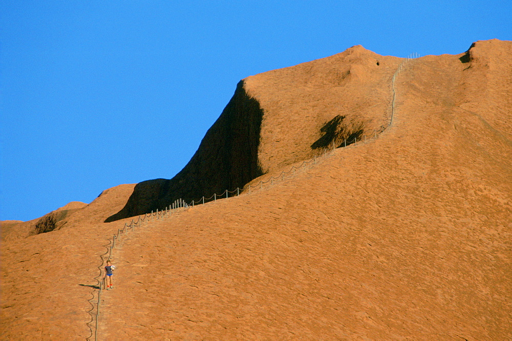 A lone visitor holding the handrail for his descent of steep Ayers Rock, Australia