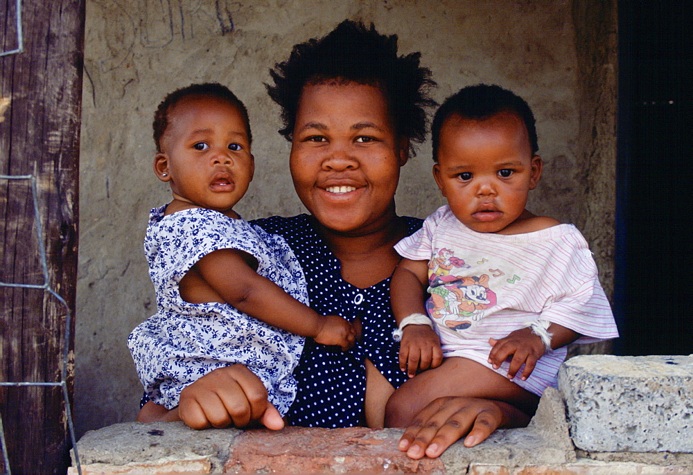 A smiling  mother holds her two children in the township of Soweto, South Africa