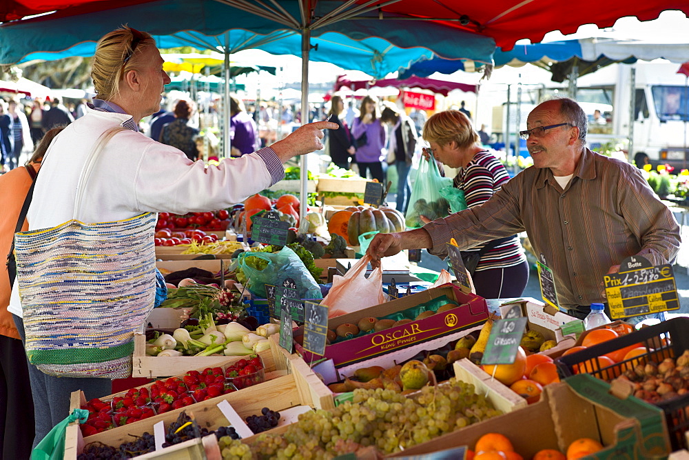 Frenchman serving customer at fruit staff at food market at Esplanade  des Quais in La Reole, Bordeaux region, France