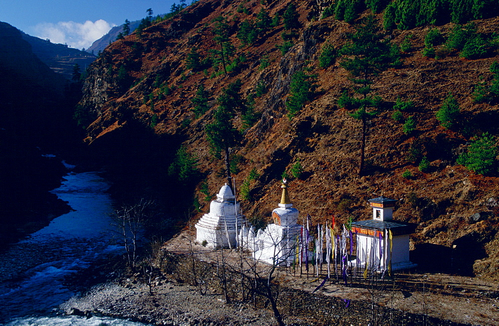 Buddhist shrines and prayer flags at the river's edge in a valley in Bhutan.