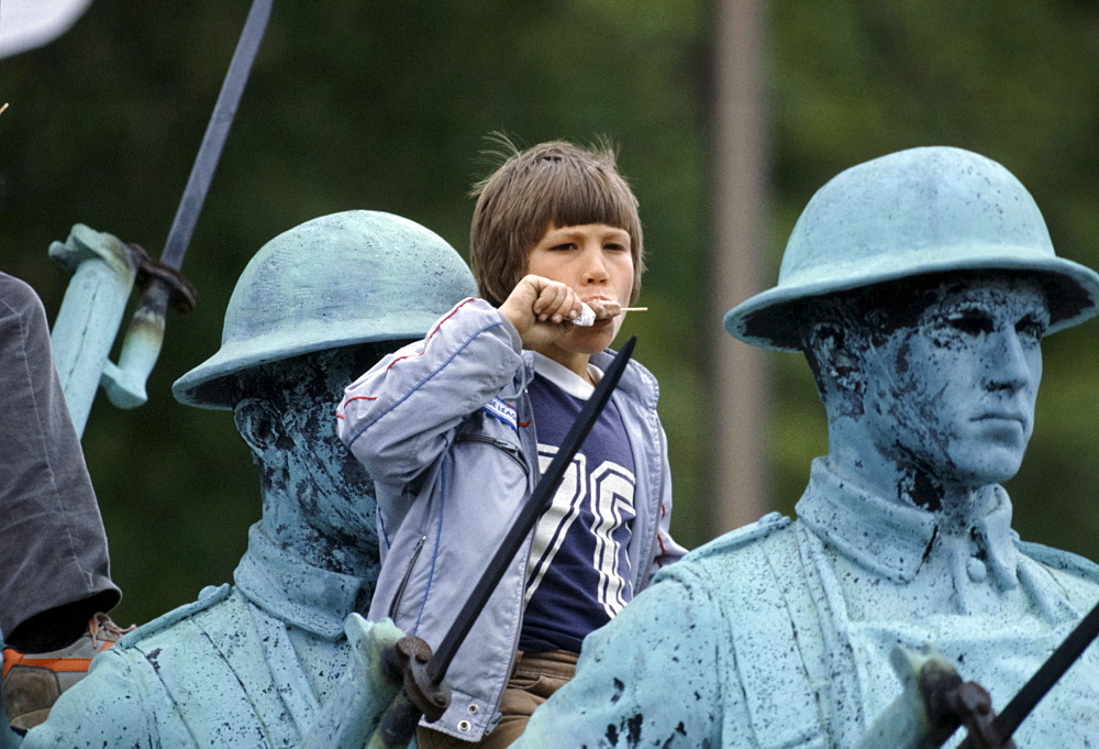 Canadian child eating ice lolly while watching parade from vantage point on Charlottetown war memorial, Canada