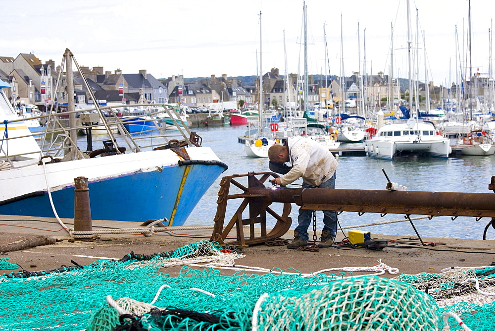 Welder at work at boatyard at Channel port of St Vaast La Hougue in Normandy, France