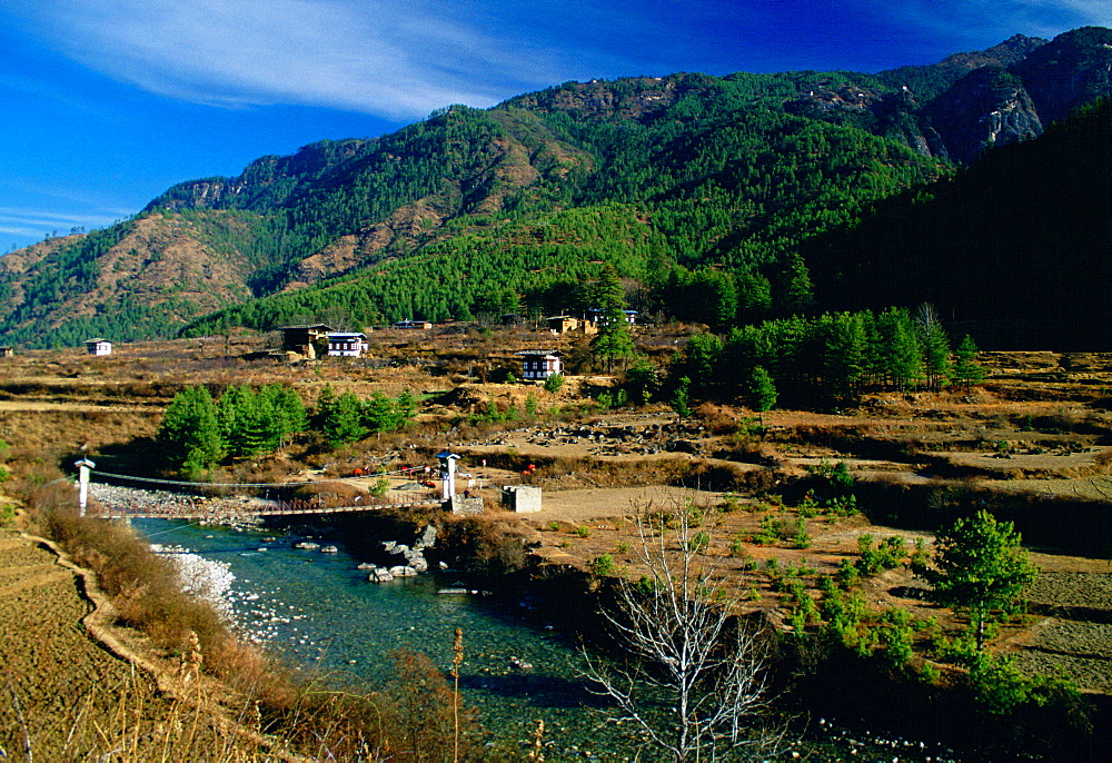 Homes at the foot of mountains in Bhutan. Bridge crossing the river.