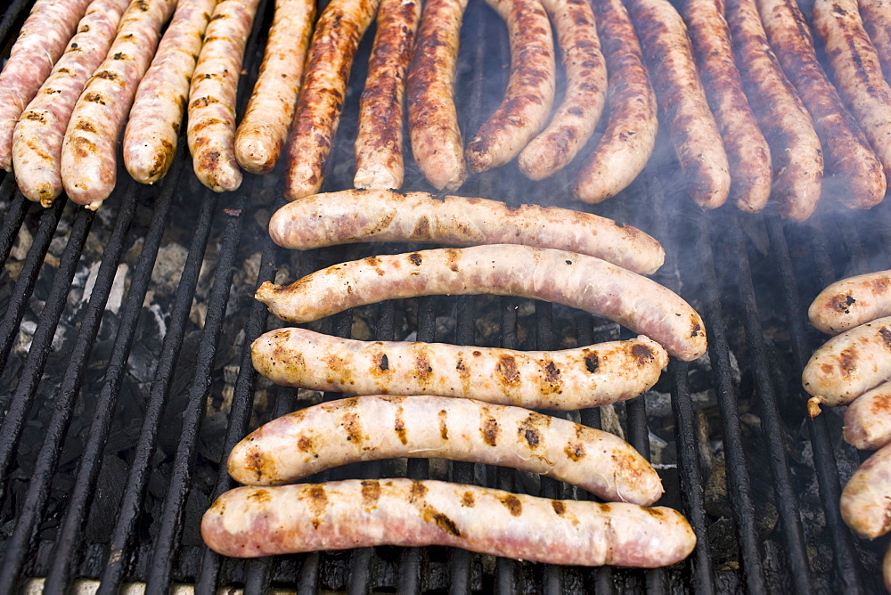 Barbecued sausages saucissons being cooked on griddle for sale as snack food at farmers market in Normandy, France