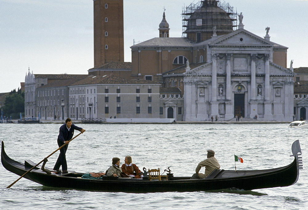 Tourists taking gondola ride propelled by gondolier along canal in Venice, Italy