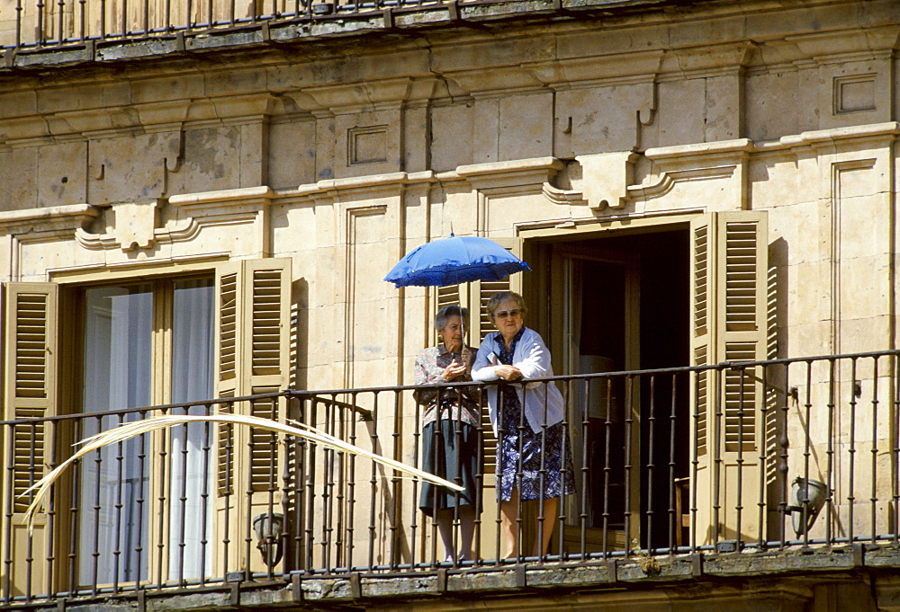 Elderly women watching from a balcony with umbrella for sun protection in Portugal