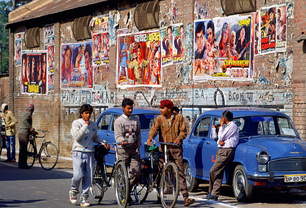 Bollywood ' film posters advertising the latest movies in Agra, India.  Young men chatting together while pushing their bicycles.