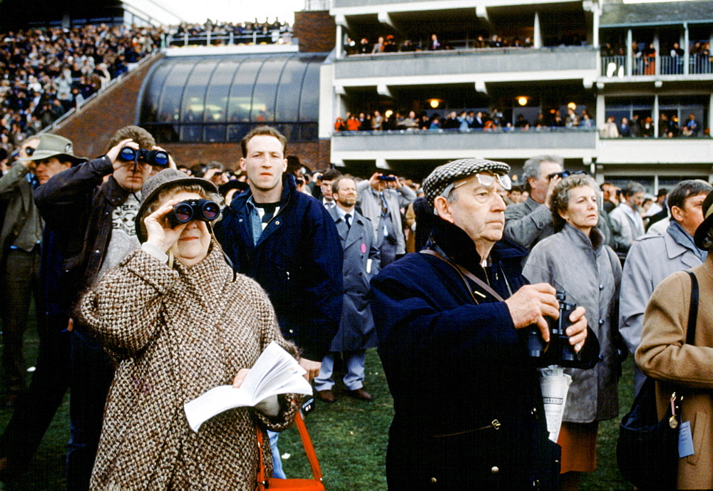 Spectactors with binoculars in front of grandstand at Cheltenham Racecourse for the National Hunt Festival of Racing, UK