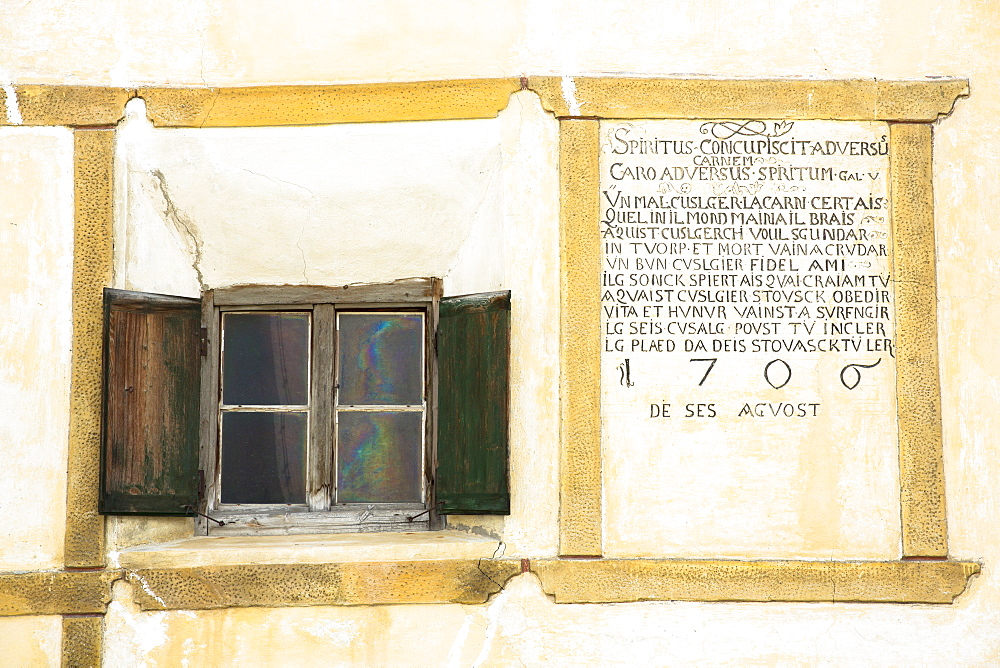 Window and inscription on old painted stone 17th century building in the Engadine Valley in the village of Guarda, Graubunden, Switzerland, Europe