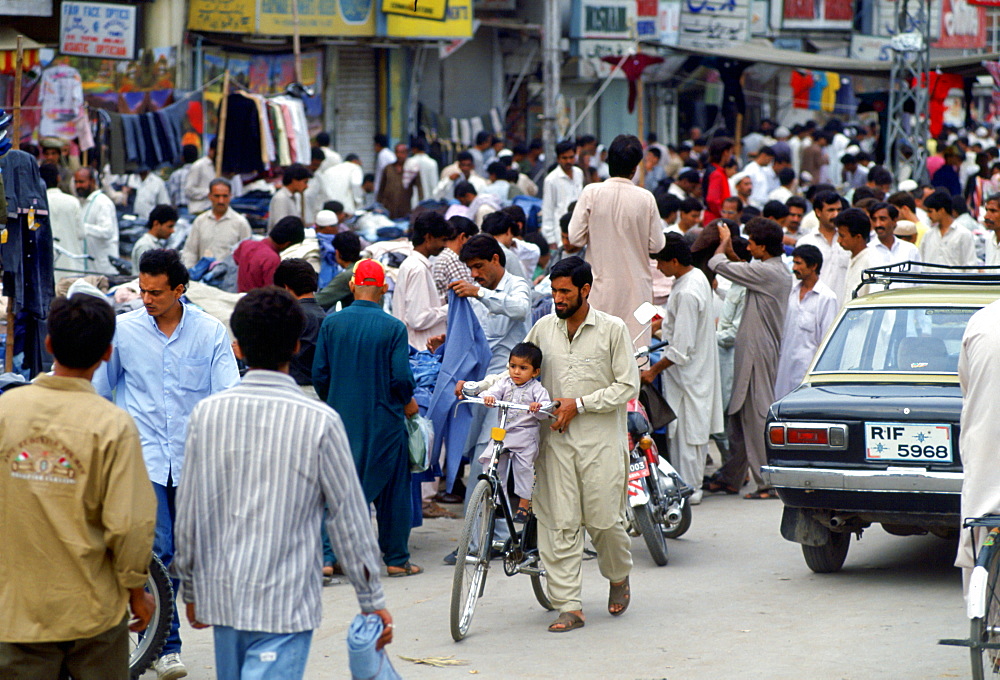 Man wheeling  child on bicycle in crowded street in Islamabad in Pakistan