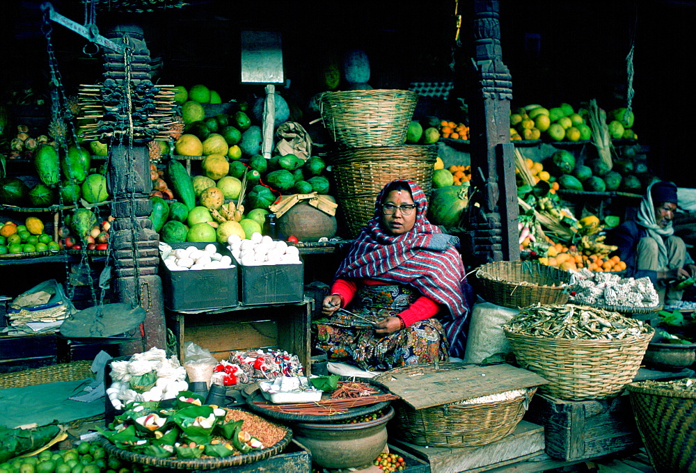 Woman stallholder holding the knife she uses to cut fruit for sale in the market in Kathmandu, Nepal.  Her stall displays in baskets fruit, vegetables and dried fish.