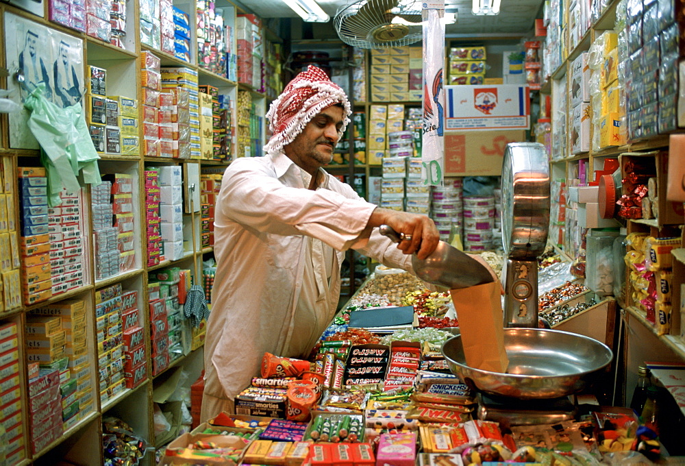 A shopkeeper in a sweet and grocery store in Kuwait City in Kuwait weighing sweets for a customer.