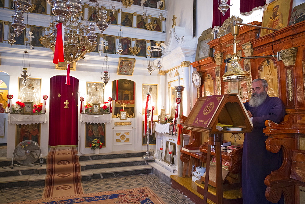 Greek Orthodox priest reading Bible inside chapel of Christian church at Krini, Corfu, Greek Islands, Greece, Europe