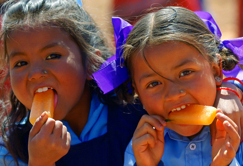 Nepalese girls (possibly sisters) enjoying orange ice lollies in rural Nepal.