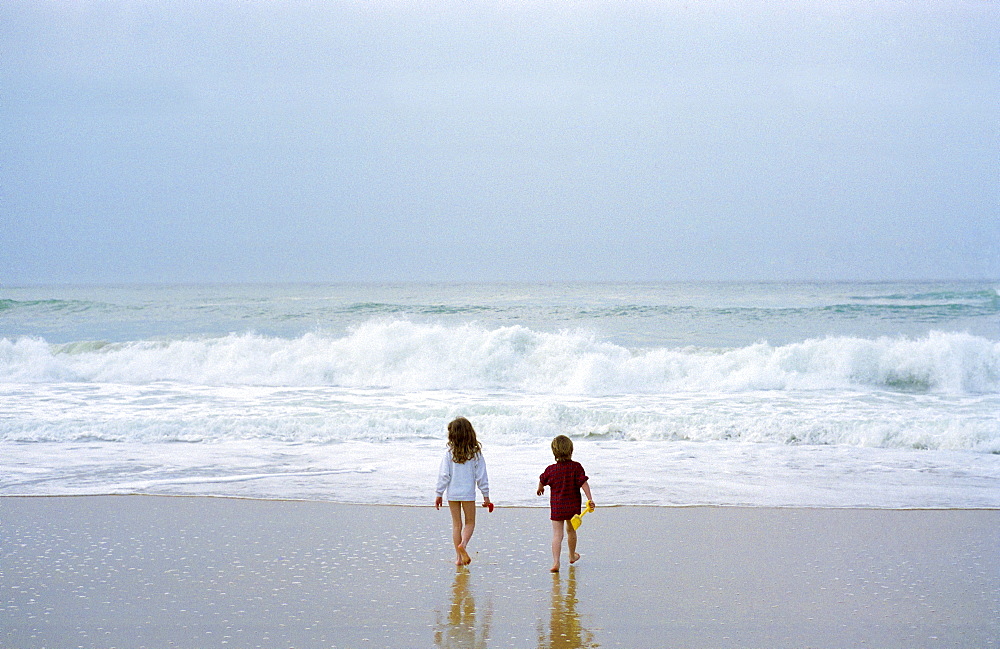 An eight year old girl and six year ld boy walking ino the sea in France