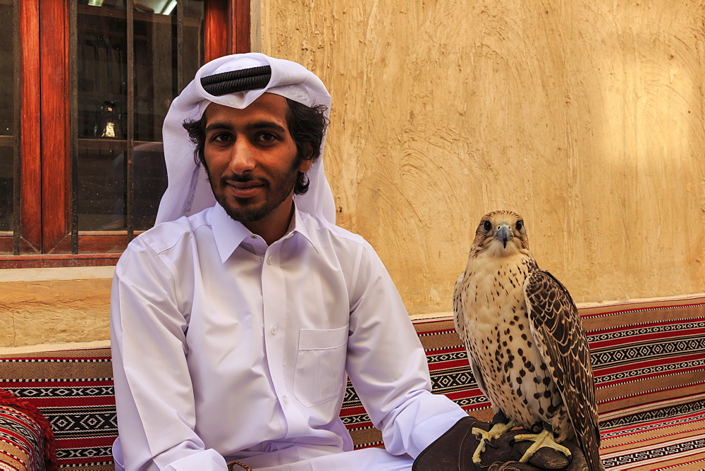 Seated man in traditional dress relaxes with his falcon at the Falcon Souq, Doha, Qatar, Middle East