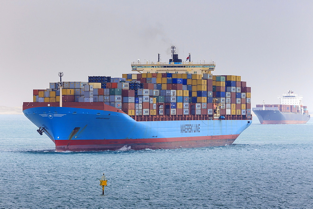 Convoy of container ships transiting the Suez Canal loom through air thick with desert sand, Great Bitter Lake, Ismalia, Egypt, Northeast Africa