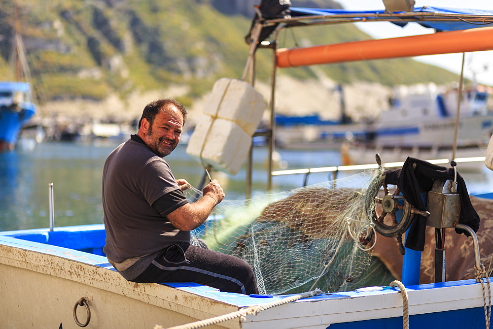 Marina Corricella harbour, smiling fisherman mending fishing nets on a boat, Procida Island, Bay of Naples, Campania, Italy, Europe