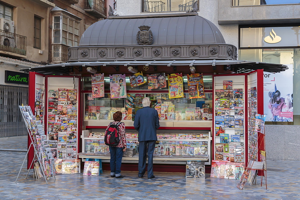 People stand at a red newspaper and magazine kiosk with fancy roof, Cartagena, Murcia Region, Spain, Europe