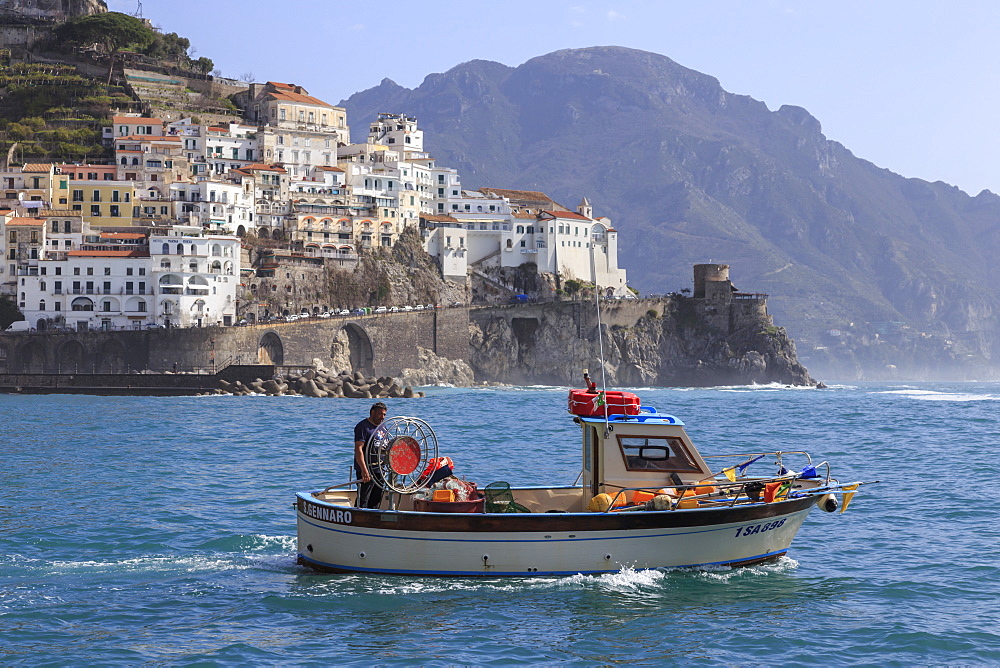 Fisherman in fishing boat heads out to sea from Amalfi harbour, with view towards Amalfi town, Costiera Amalfitana (Amalfi Coast), UNESCO World Heritage Site, Campania, Italy, Europe