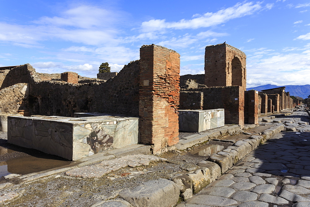 Cobbled street with thermopolium counters and arch, Roman ruins of Pompeii, UNESCO World Heritage Site, Campania, Italy, Europe