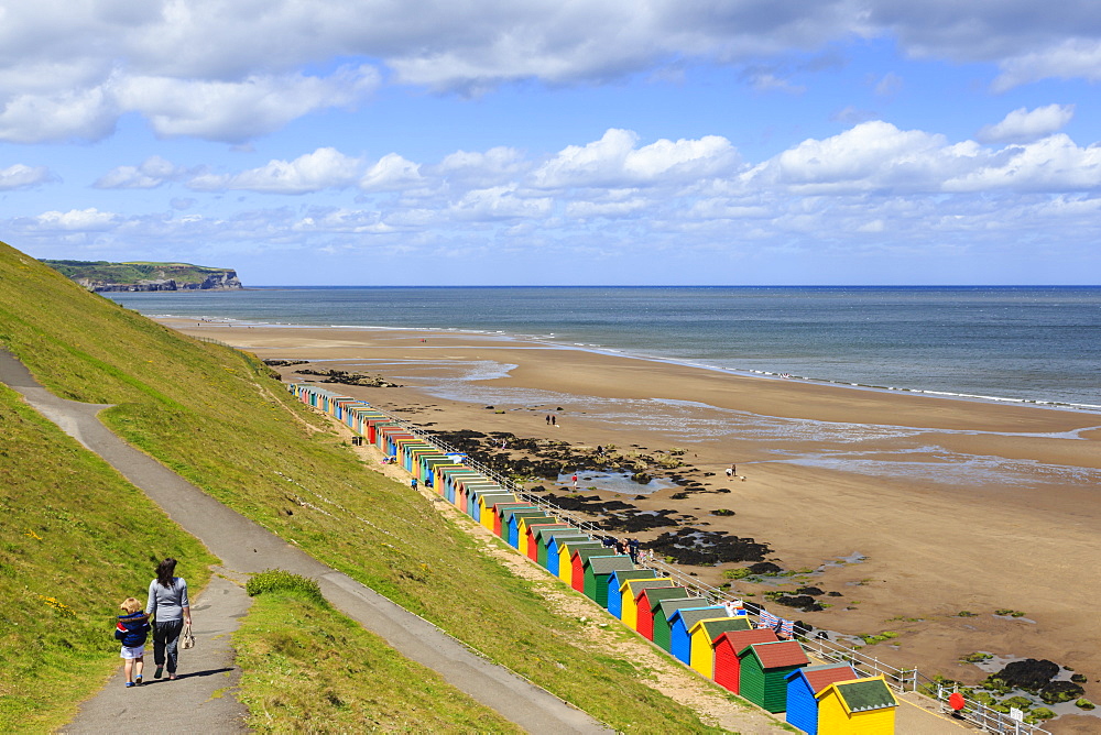 Elevated view of colourful beach huts on West Cliff Beach, mother and daughter hand in hand, Whitby, North Yorkshire, England, United Kingdom, Europe