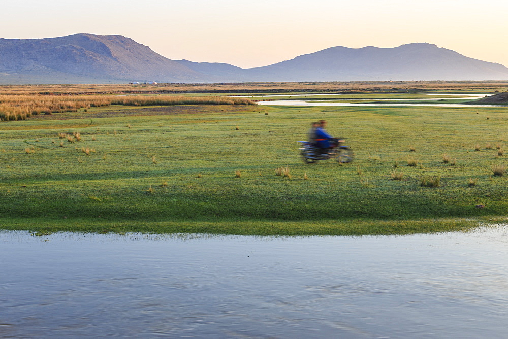 Nomads on motorcycle pass in a blur, river and distant gers, dawn, Nomad camp, Gurvanbulag, Bulgan, Northern Mongolia, Central Asia, Asia