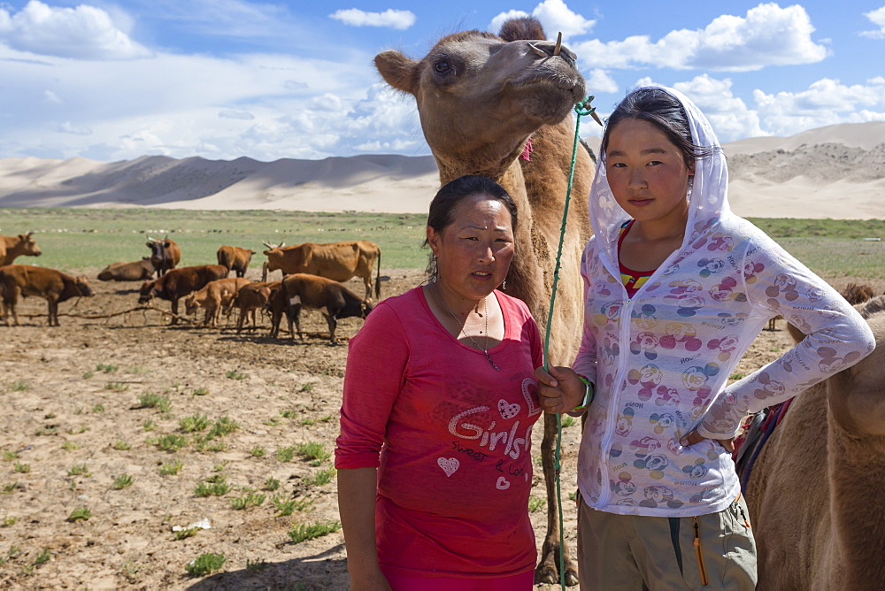 Nomadic camel herders, mother and daughter, with two hump Bactrian camel with Khongoryn Els sand dunes behind, Gobi Desert, Mongolia, Central Asia, Asia