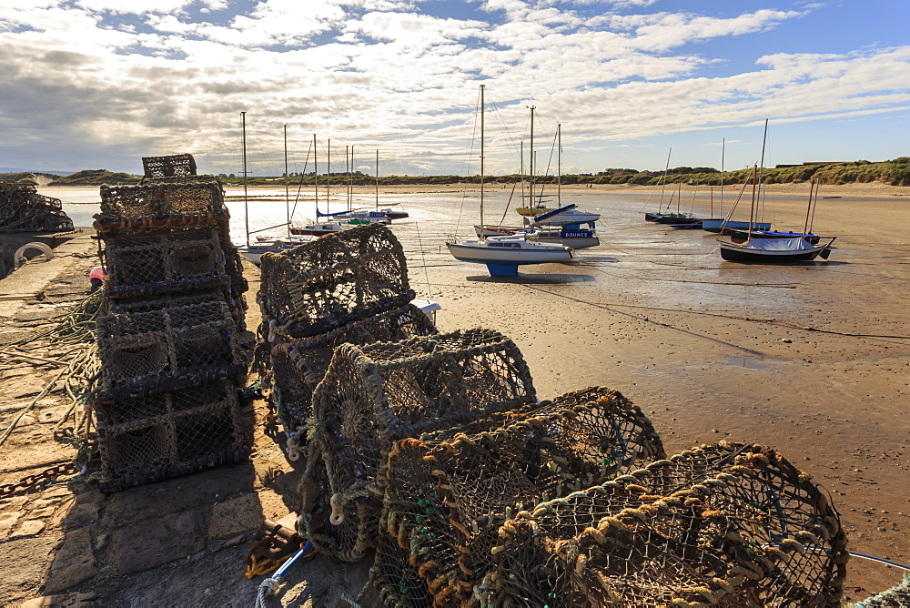 Lobster pots on harbour wall and yachts on beach at low tide on a summer evening, Beadnell, Northumberland, England, United Kingdom, Europe