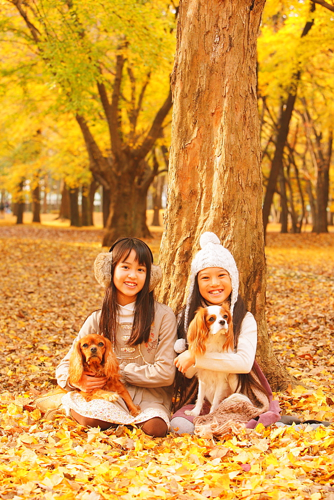 Girls Holding Their Dog In Leaves