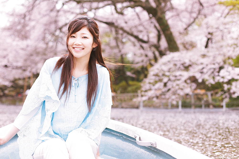 Woman In Rowing Boat On Lake With Cherry Blossom In Background