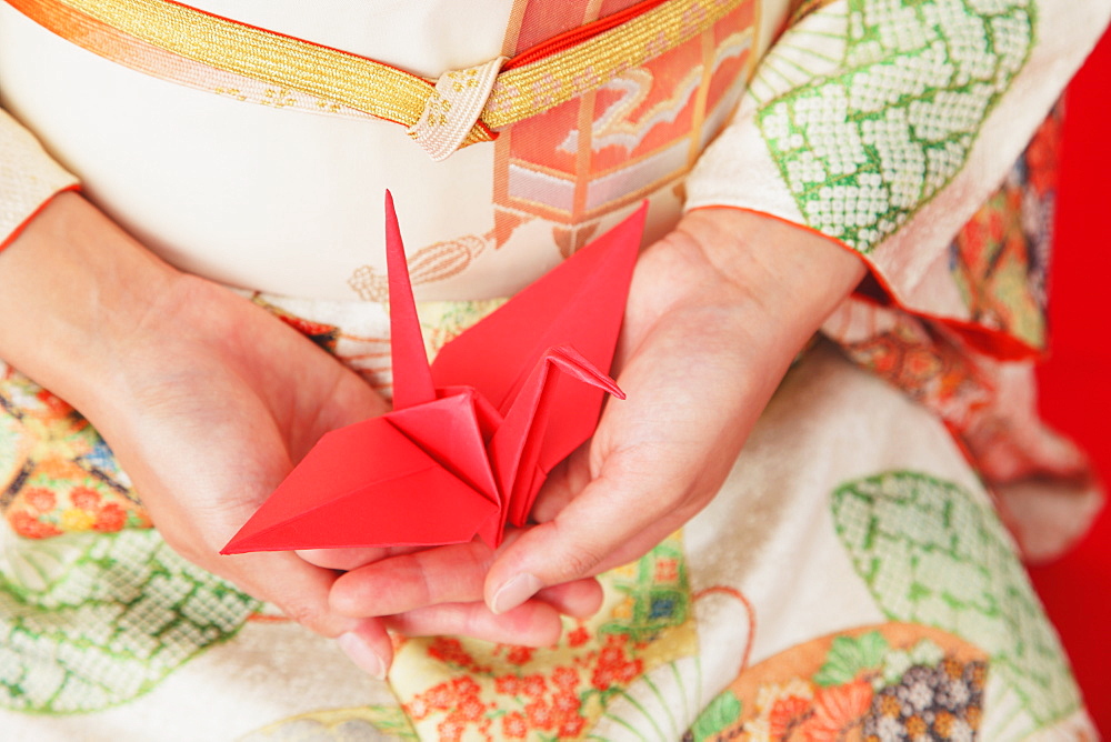 Close up of a Japanese woman in a kimono holding an origami of a crane