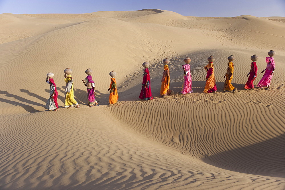 Women bear the responsibility of fetching water from the sparse wells within Rajasthan's vast Thar Desert. Trekking up the side of a sand dune, women expertly balance large clay water vessels atop their heads. Rajasthan, India, Thar Desert, Rajasthan, India