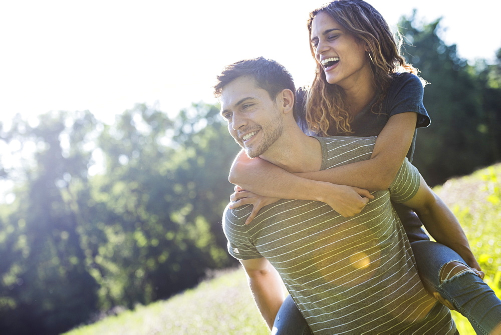 A couple, a man giving a young woman a piggyback, walking through a flower meadow in summer.