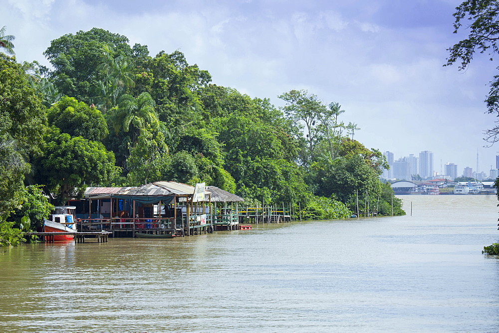 Boats and stilt house on an igarape (flooded creek) in the Brazilian Amazon with Belem city behind, Para, Brazil, South America