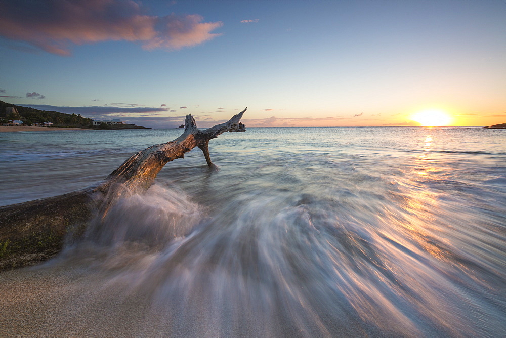 Waves on a tree trunk on the beach framed by the Caribbean sunset, Hawksbill Bay, Antigua, Antigua and Barbuda, Leeward Islands, West Indies, Caribbean, Central America