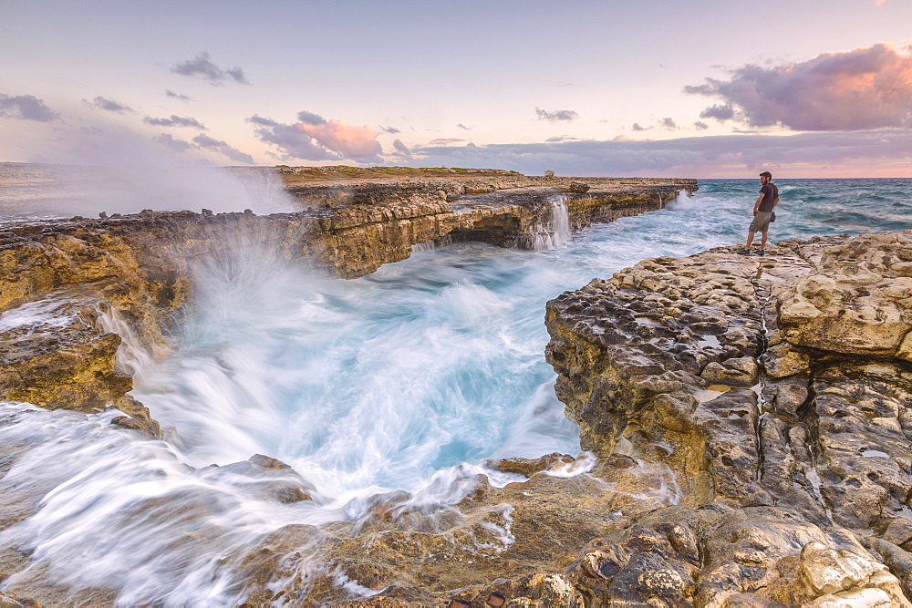 Hiker on the cliffs admires the crashing waves at Devil's Bridge, Antigua, Antigua and Barbuda, Leeward Islands, West Indies, Caribbean, Central America