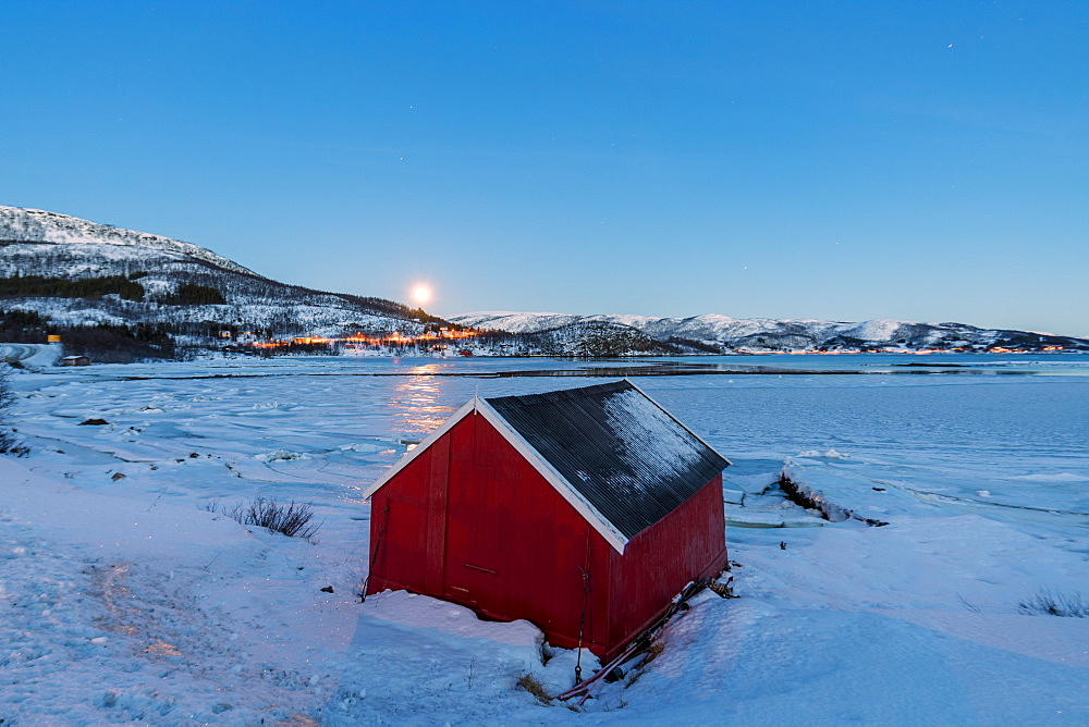 The blue light of dusk on the typical house of fishermen framed by the frozen sea, Fjordbotn, Senja, Troms County, Norway, Scandinavia, Europe